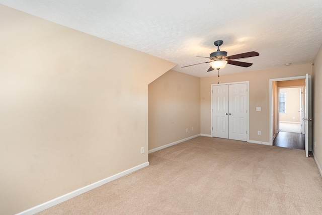 unfurnished bedroom featuring a textured ceiling, light colored carpet, a ceiling fan, baseboards, and a closet