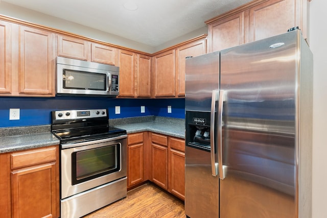 kitchen featuring appliances with stainless steel finishes, dark countertops, and light wood-style flooring