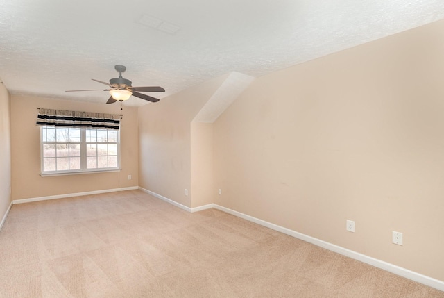 spare room with light colored carpet, ceiling fan, a textured ceiling, and baseboards