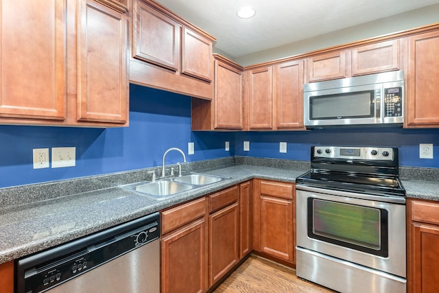 kitchen featuring dark countertops, appliances with stainless steel finishes, light wood-type flooring, a sink, and recessed lighting