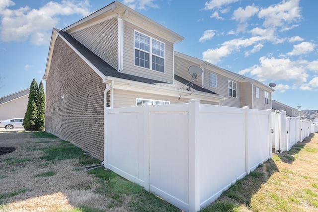 view of side of home featuring fence, a lawn, and brick siding