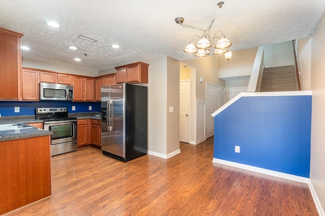 kitchen with stainless steel appliances, dark countertops, brown cabinetry, and light wood-style floors