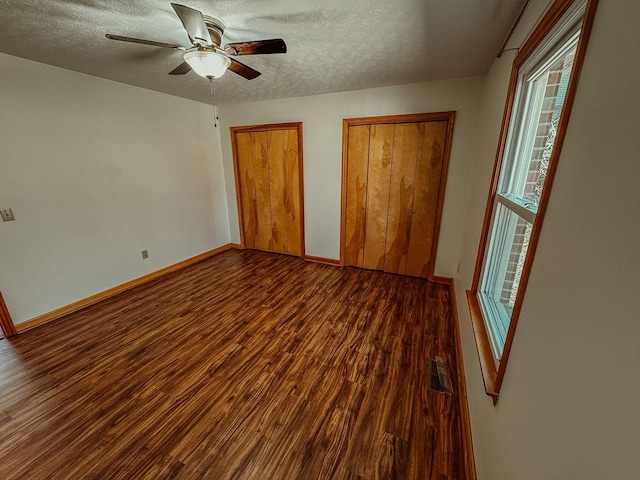 unfurnished bedroom featuring wood finished floors, visible vents, baseboards, a textured ceiling, and two closets