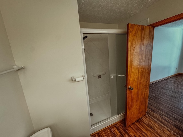 full bathroom featuring toilet, wood finished floors, a stall shower, and a textured ceiling