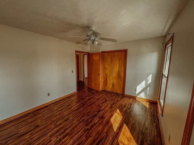 unfurnished bedroom featuring a ceiling fan, a textured ceiling, dark wood-style floors, a closet, and baseboards