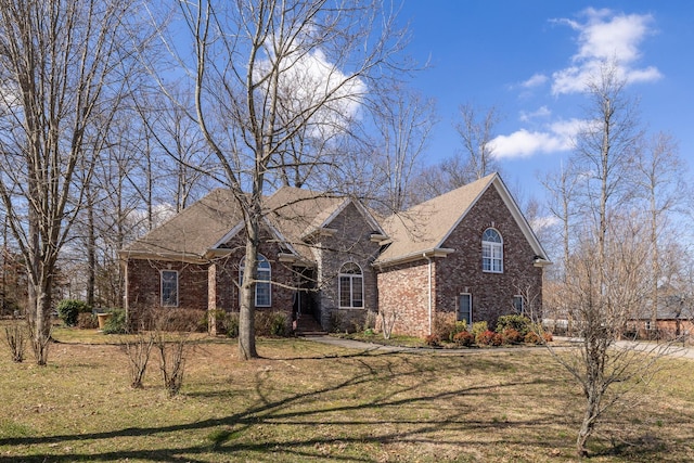 view of front of property featuring a shingled roof, brick siding, and a front lawn