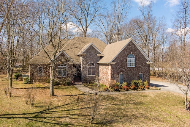 traditional home with brick siding, a front yard, and a shingled roof