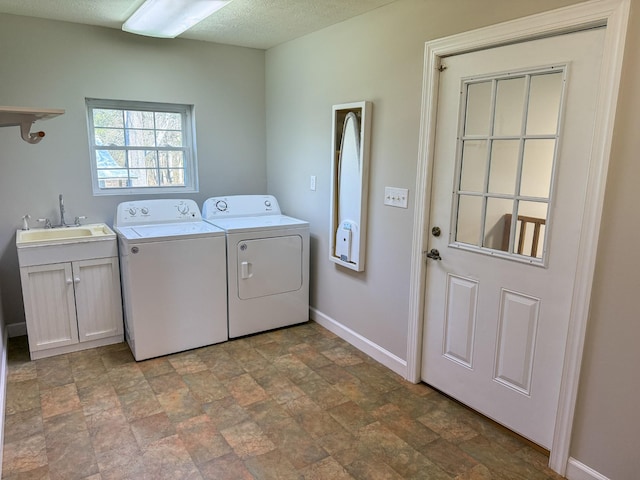 laundry room featuring baseboards, washer and clothes dryer, cabinet space, a textured ceiling, and a sink