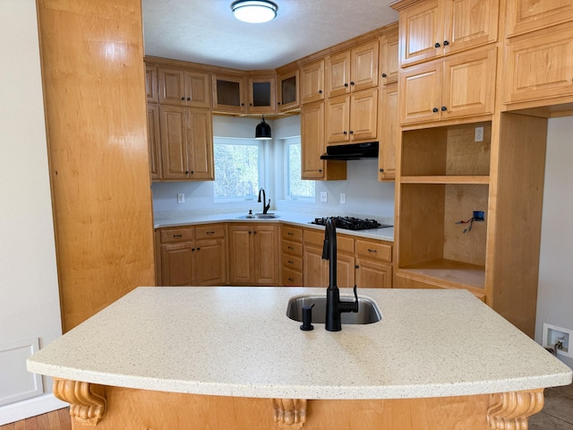 kitchen with under cabinet range hood, black gas stovetop, light stone counters, and a sink