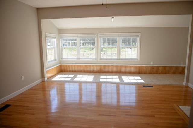 empty room featuring visible vents, lofted ceiling, baseboards, and wood finished floors