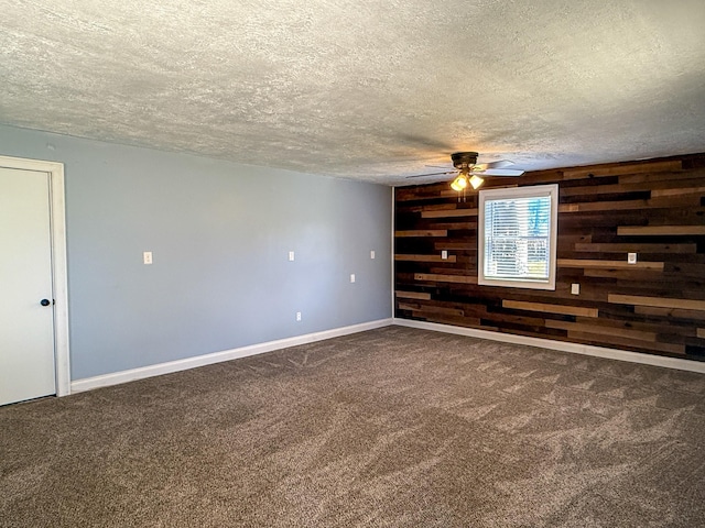 carpeted empty room with ceiling fan, baseboards, a textured ceiling, and wood walls