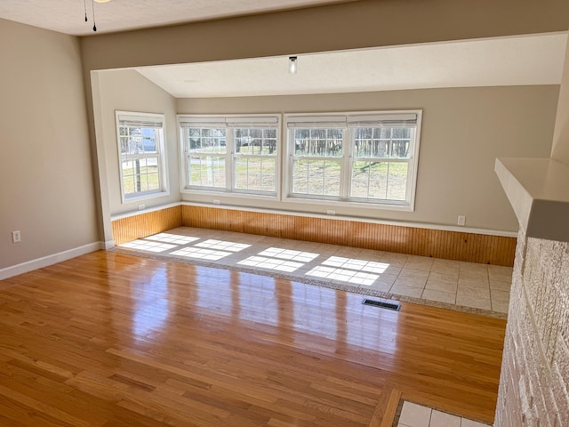 spare room featuring lofted ceiling, wood finished floors, visible vents, and a wealth of natural light