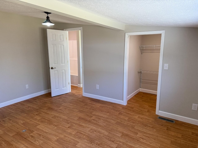 unfurnished bedroom featuring baseboards, visible vents, a textured ceiling, and light wood-style floors