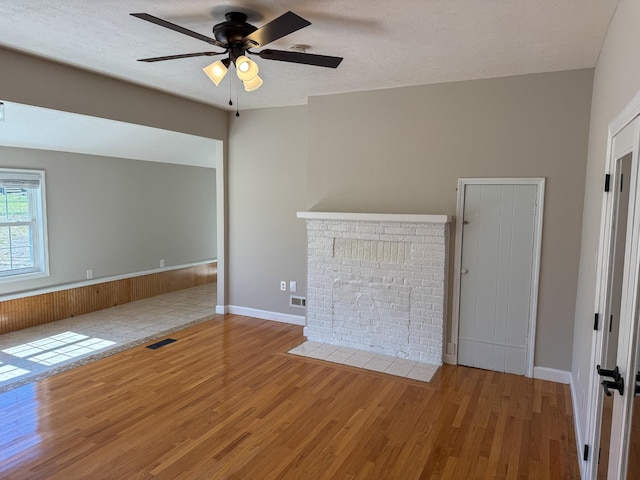 unfurnished living room featuring visible vents, a textured ceiling, a brick fireplace, and wood finished floors