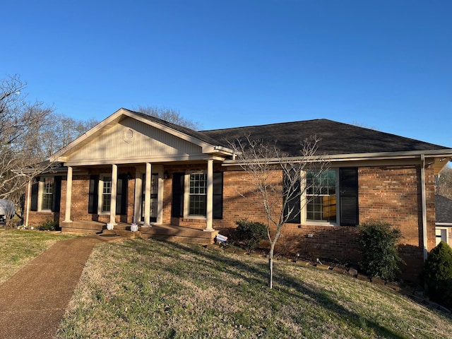 view of front of property featuring brick siding, covered porch, and a front yard