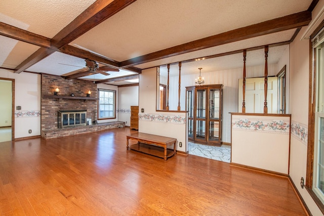 unfurnished living room with ceiling fan, beam ceiling, a fireplace, wood finished floors, and a textured ceiling