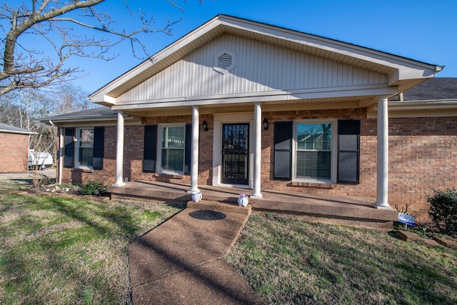 view of front of property featuring a front yard, brick siding, and covered porch