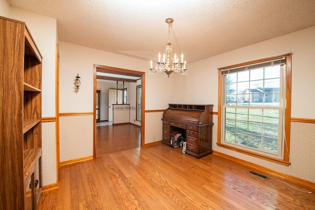 dining area featuring a wainscoted wall, visible vents, wallpapered walls, an inviting chandelier, and light wood-style floors