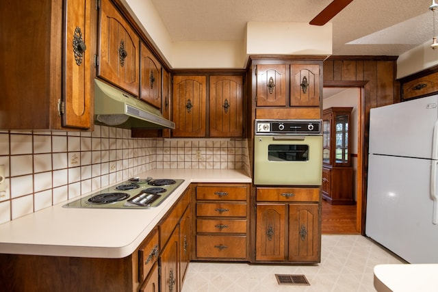 kitchen featuring visible vents, under cabinet range hood, tasteful backsplash, white appliances, and light countertops