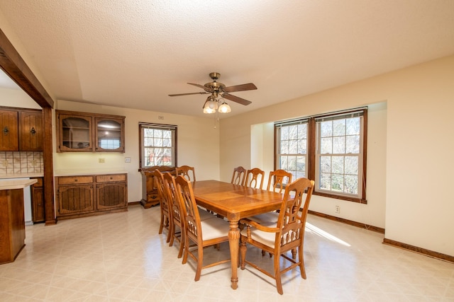 dining room featuring a textured ceiling, light floors, baseboards, and ceiling fan