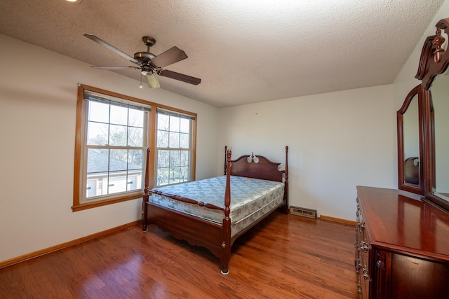 bedroom featuring visible vents, a textured ceiling, baseboards, and wood finished floors