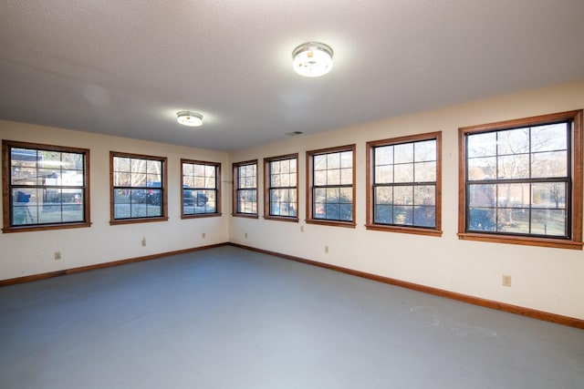 spare room with a textured ceiling, baseboards, and finished concrete flooring