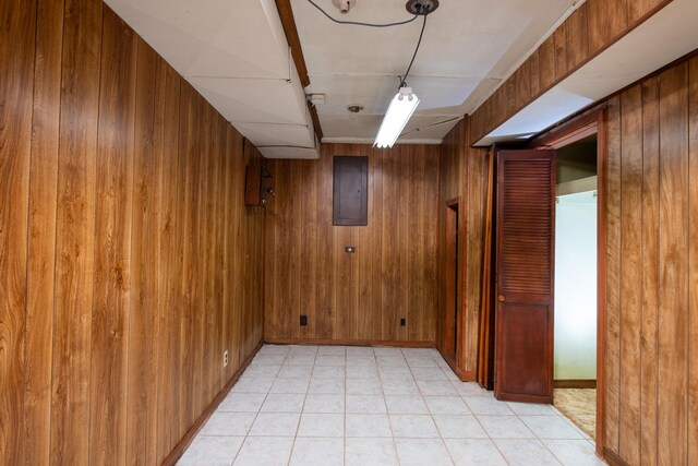 finished below grade area featuring wooden walls, electric panel, light tile patterned flooring, and baseboards