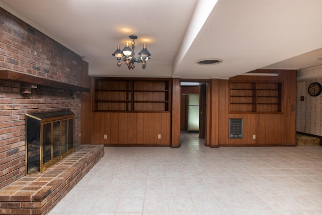 unfurnished living room featuring wooden walls, heating unit, visible vents, a brick fireplace, and a chandelier