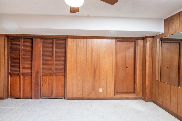 interior details featuring wooden walls, ceiling fan, and a textured ceiling