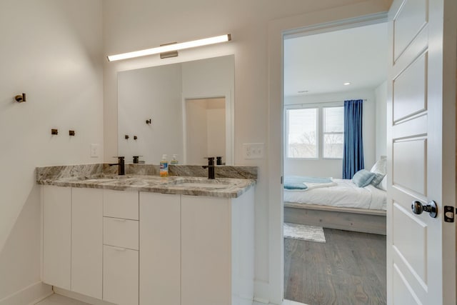 ensuite bathroom featuring connected bathroom, double vanity, a sink, and wood finished floors