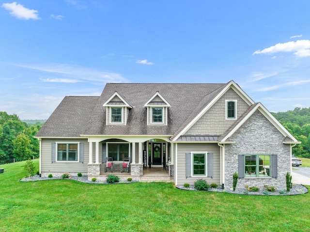 view of front of home with covered porch, stone siding, a front lawn, and a shingled roof