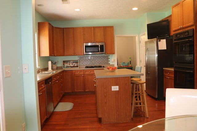 kitchen featuring dark wood finished floors, a kitchen bar, decorative backsplash, a kitchen island, and black appliances