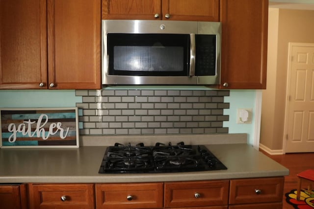 kitchen featuring brown cabinets, black gas cooktop, light countertops, stainless steel microwave, and decorative backsplash