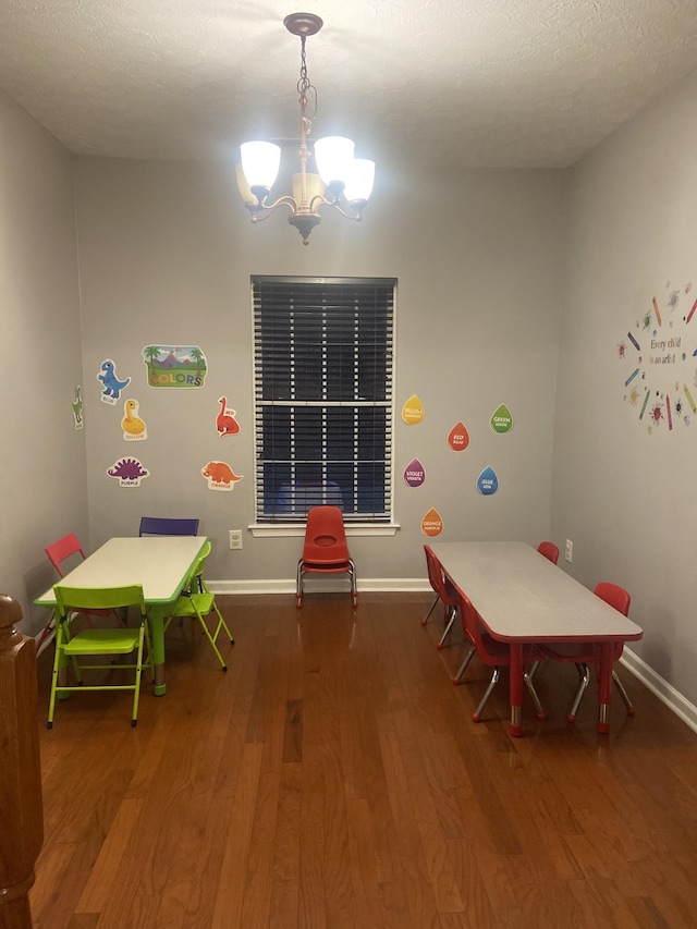 playroom with a notable chandelier, a textured ceiling, baseboards, and wood finished floors