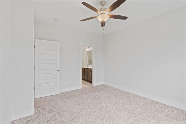 unfurnished bedroom featuring light carpet, ensuite bath, baseboards, and a ceiling fan