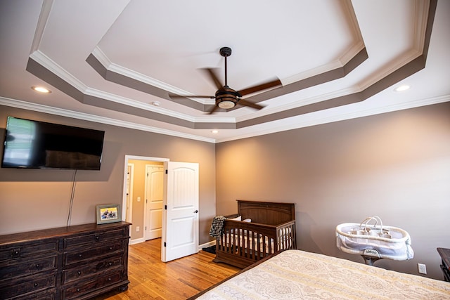 bedroom with ornamental molding, a raised ceiling, wood finished floors, and recessed lighting