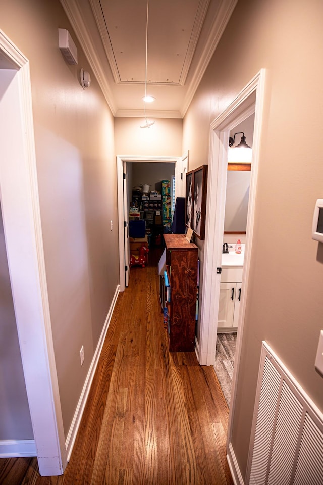 hall with wood finished floors, visible vents, baseboards, ornamental molding, and attic access