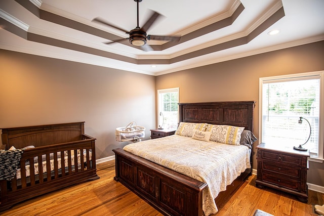 bedroom with ornamental molding, a tray ceiling, light wood-style flooring, and baseboards