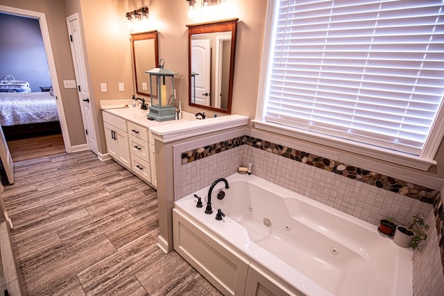 ensuite bathroom with connected bathroom, a sink, wood finished floors, a jetted tub, and double vanity