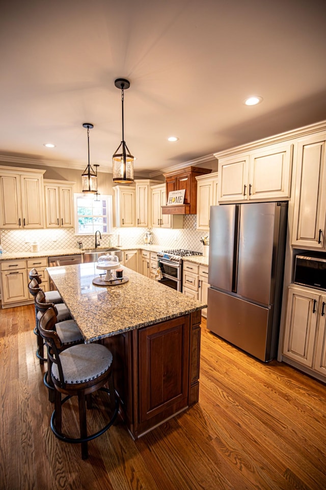 kitchen featuring a center island, stainless steel appliances, tasteful backsplash, a sink, and wood finished floors