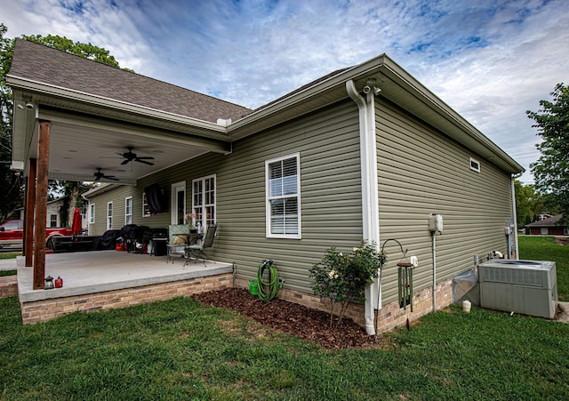 view of side of property featuring ceiling fan, a patio, central AC, roof with shingles, and a lawn