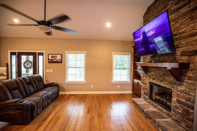 living room featuring a ceiling fan, a stone fireplace, baseboards, and wood finished floors