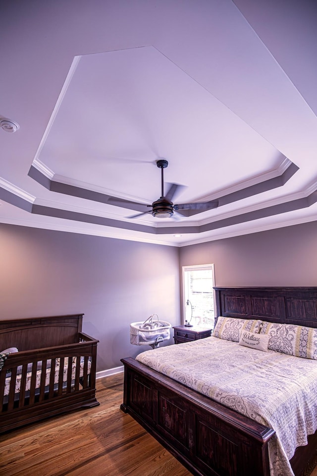 bedroom featuring dark wood-style floors, a ceiling fan, a tray ceiling, and crown molding