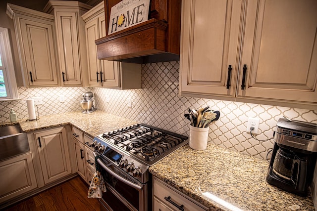 kitchen with range with two ovens, backsplash, cream cabinets, light stone countertops, and premium range hood