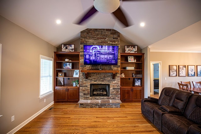 living room with ceiling fan, lofted ceiling, a stone fireplace, wood finished floors, and baseboards