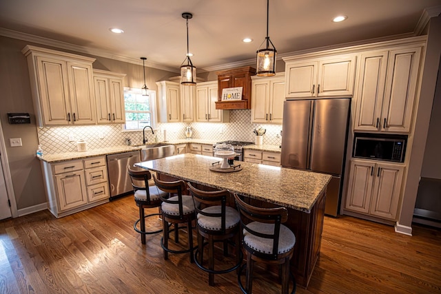 kitchen with dark wood-style floors, stainless steel appliances, ornamental molding, a kitchen island, and light stone countertops