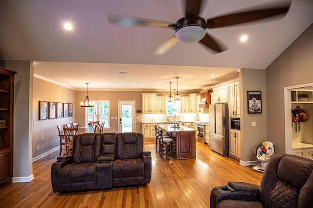 living room with light wood-type flooring, crown molding, baseboards, and ceiling fan with notable chandelier