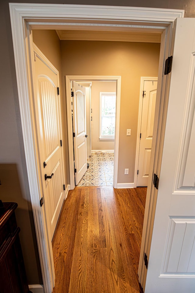 corridor featuring crown molding, baseboards, and wood finished floors