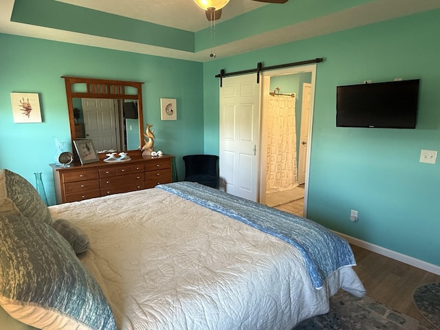 bedroom with a tray ceiling, wood finished floors, baseboards, and a barn door