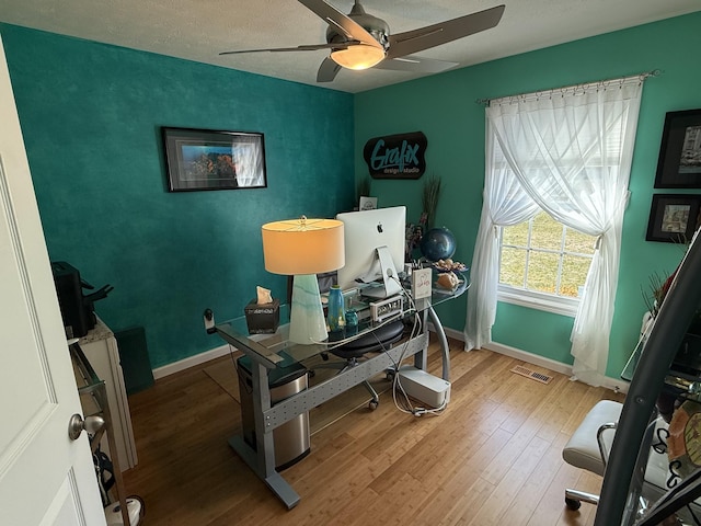 office space featuring ceiling fan, a textured ceiling, wood finished floors, visible vents, and baseboards